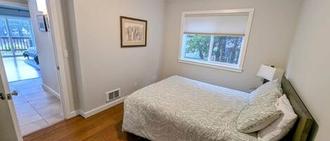 A bedroom with a bed, a window, a door, and a framed picture on the wall.