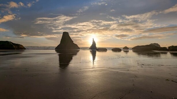 Une plage avec de grandes formations rocheuses et le soleil se couchant à l’horizon.