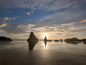A beach with large rock formations and the sun setting in the background. - Bandon Seaside Escape (Bandon)