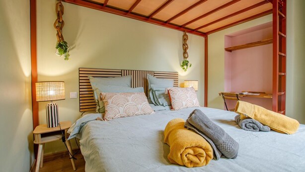 A neatly made bed with pillows and a blanket, a bedside table with a lamp, and a wooden headboard.
