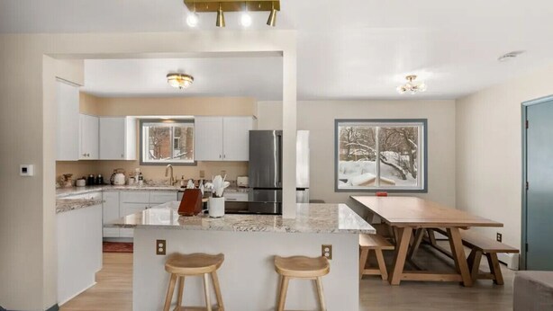 Een moderne keuken met een centraal eiland, houten krukken, een eettafel en een groot raam met uitzicht op sneeuw.