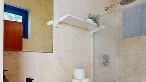 Un baño con lavabo blanco, inodoro y ducha. Hay un espejo sobre el lavabo y una toalla colgada en la pared.