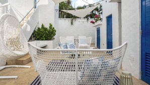 Una silla de mimbre blanca, un sofá de mimbre blanco y una mesita con cojines de estampado azul y blanco.
