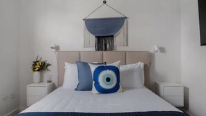 Un dormitorio ordenado con una cama, dos mesitas de noche, un macramé en la pared y un jarrón con flores.
