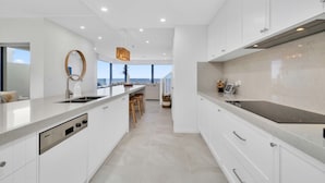 A modern kitchen with white cabinetry, a large island with stools, and a view to the outside. - Three-Bedroom Luxurious Beachfront Holiday Home (North Brighton)