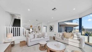 A spacious living room with two white sofas, a round coffee table, and a large window offering a view of the sea. - Three-Bedroom Luxurious Beachfront Holiday Home (North Brighton)