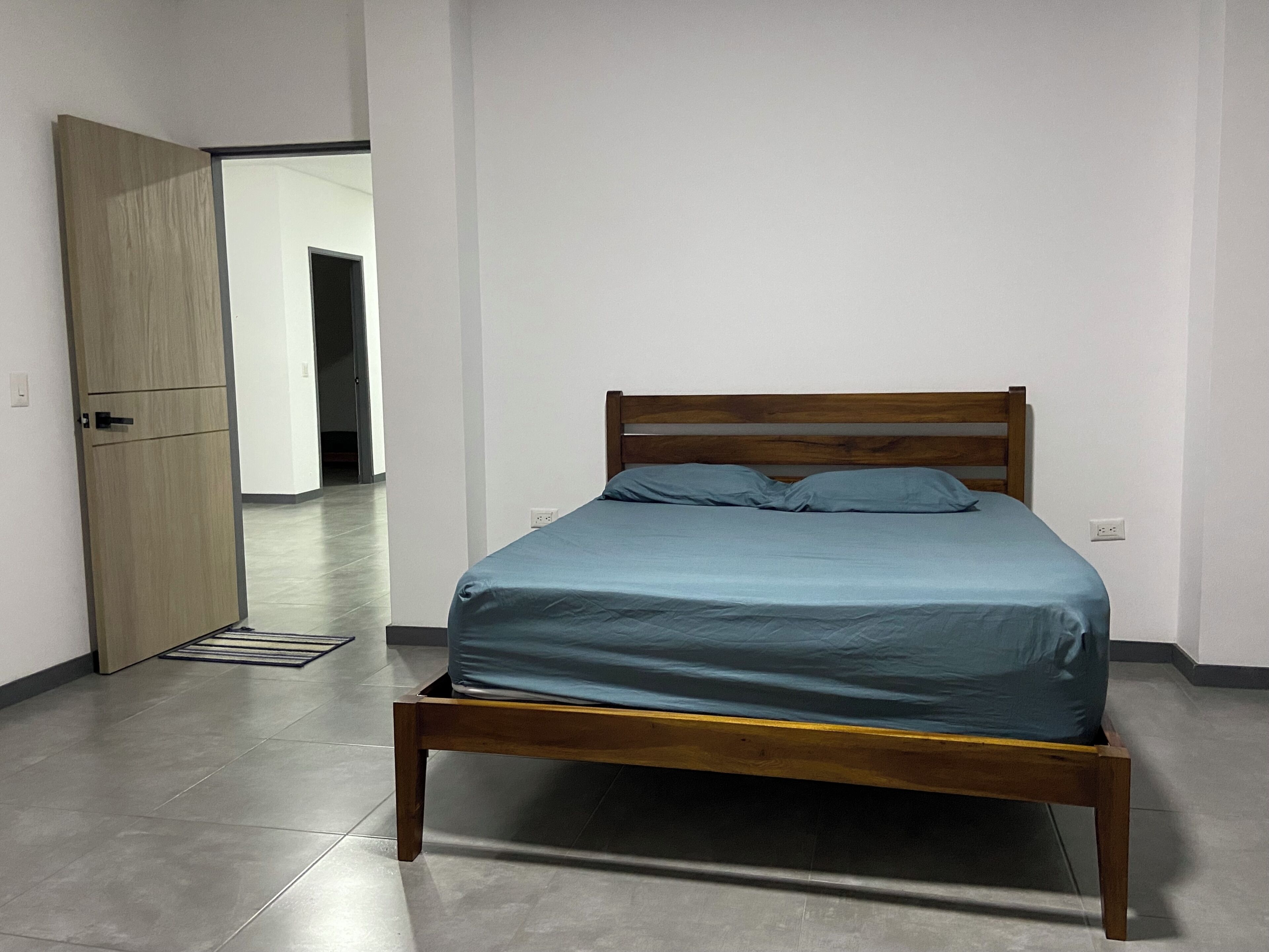 A bedroom with a wooden bed frame, a blue mattress, and a wooden wardrobe.