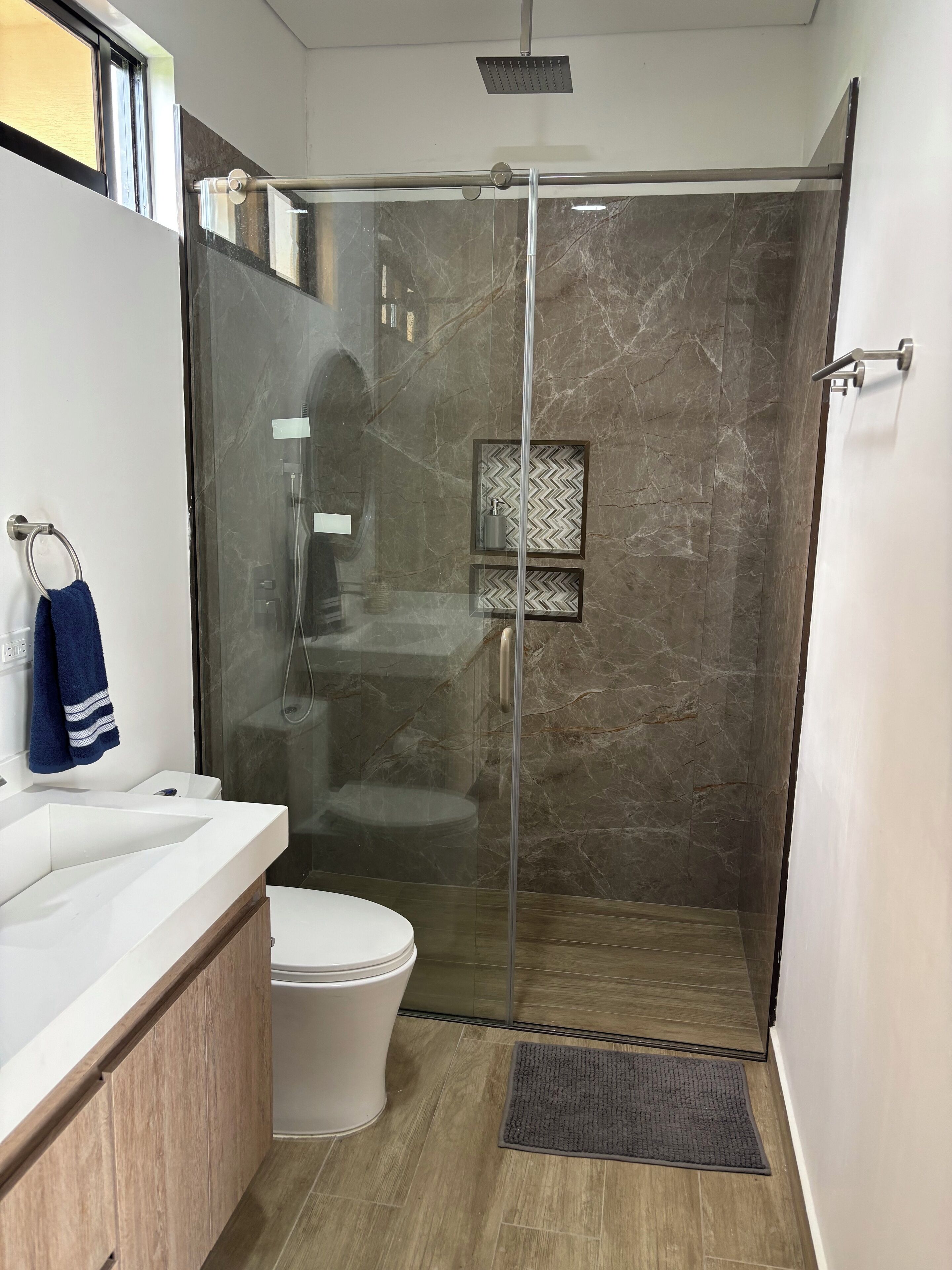 Un baño moderno con ducha de vidrio, lavamanos blanco y un inodoro.