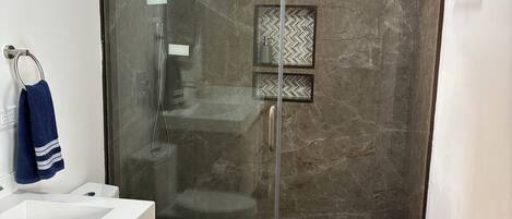 Un baño moderno con ducha de vidrio, lavamanos blanco y un inodoro.