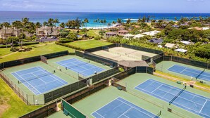 Un complexe de courts de tennis comprenant plusieurs terrains, entouré d’une végétation luxuriante et offrant une vue sur l’océan.