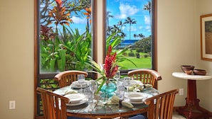 Une table à manger dressée pour quatre personnes, avec vue sur un paysage tropical grâce à de grandes fenêtres.