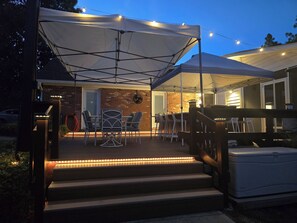 A covered outdoor patio with a table and chairs, a brick wall, and a staircase leading to a door. - 2026 Masters Rental in Aiken, SC. (Aiken)