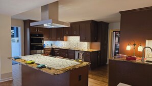 Une cuisine moderne avec des meubles en bois foncé, un grand îlot central doté d’un plan de travail à motifs et une hotte de cuisine en acier inoxydable.