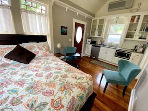 Un dormitorio con cama, una silla, escritorio y kitchenette.