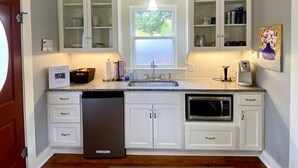 A kitchen with white cabinetry, a built-in microwave, a dishwasher, and a window with a view of greenery. - Quaint Historical Southtown - La Casita on Simon (San Antonio)