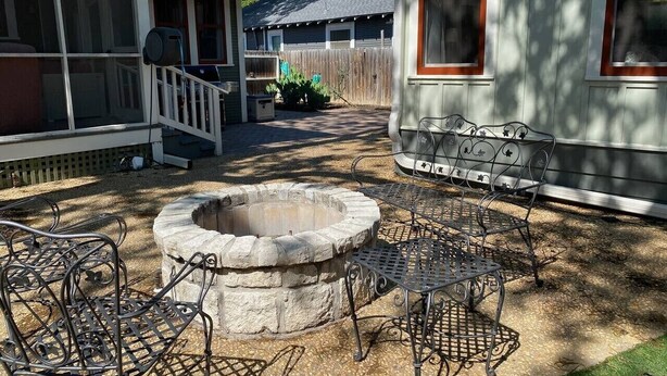 A backyard with a stone fire pit, metal chairs, a covered porch, and a wooden fence. - Quaint Historical Southtown - La Casita on Simon (San Antonio)