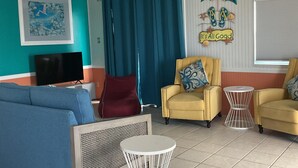 Un salon avec un canapé, deux fauteuils, un téléviseur et un ventilateur de plafond.