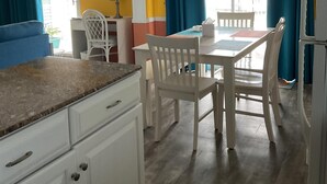 Une pièce comprenant une table à manger, des chaises, un ventilateur de plafond et une fenêtre avec des rideaux.