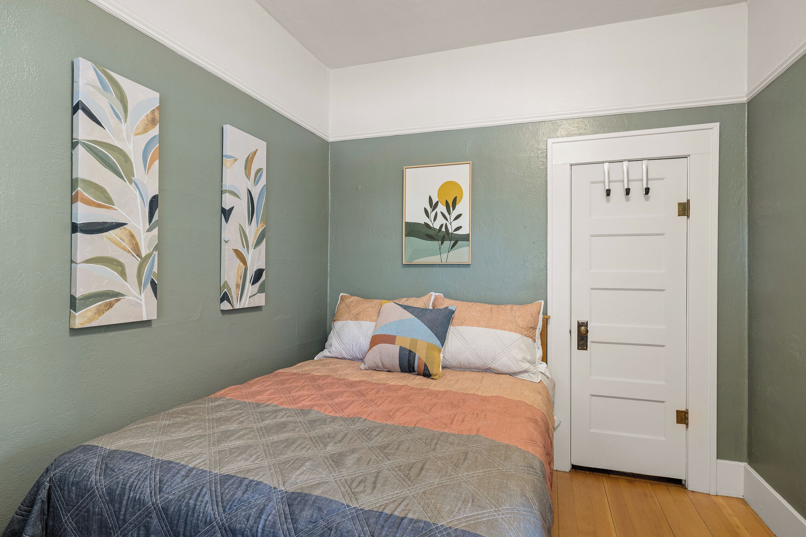 Une chambre à coucher avec un lit, deux tableaux accrochés au mur, une porte et une petite fenêtre.