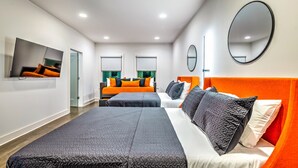 Una habitación de hotel moderna con una cama grande, dos camas más pequeñas, un televisor y un espejo.