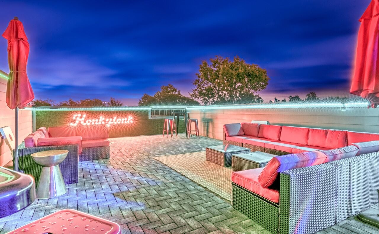 A rooftop patio with wicker furniture, a neon sign, and string lights.
