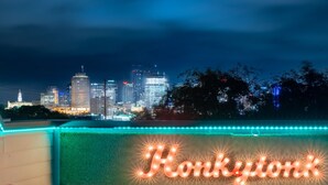 Un horizonte urbano nocturno con edificios iluminados y un letrero de neón que dice "Honkytonk" en la azotea.
