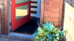 Una puerta roja con un panel de vidrio, una pared de madera con un cartel con el número '615', y una escalera que da al interior.