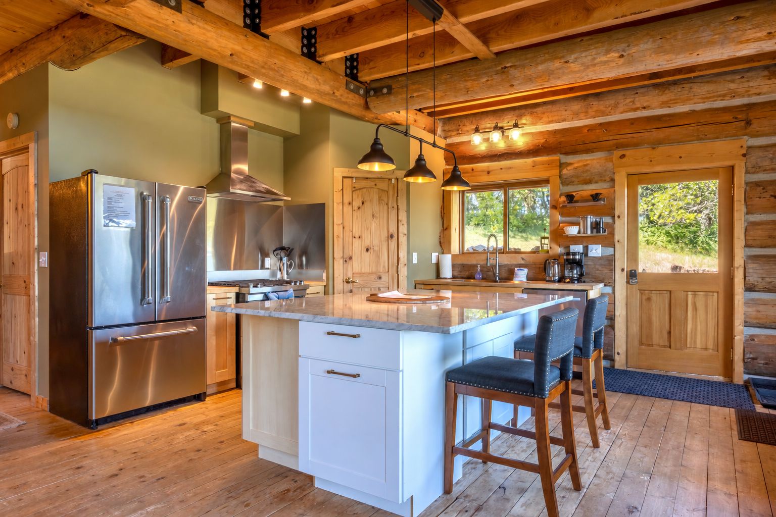 Una cocina moderna con electrodomésticos de acero inoxidable, una isla central con taburetes y vigas de madera en el techo.