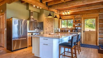 Una cocina moderna con electrodomésticos de acero inoxidable, una isla central con taburetes y vigas de madera en el techo.
