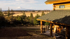 A log cabin with a covered porch, a view of a mountain, and a natural landscape.