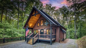 A log cabin with a wooden deck, a staircase, and an American flag. - Modern Rustic 3BR & Loft, Hot Tub, GR and Fire Pit (Ellijay)