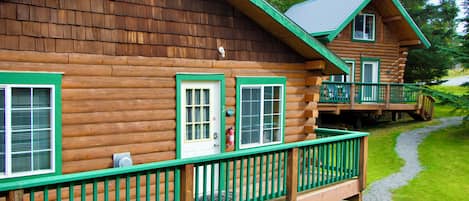 Eine Holzhütte mit einer grünen Veranda und einem Balkon im zweiten Stock.