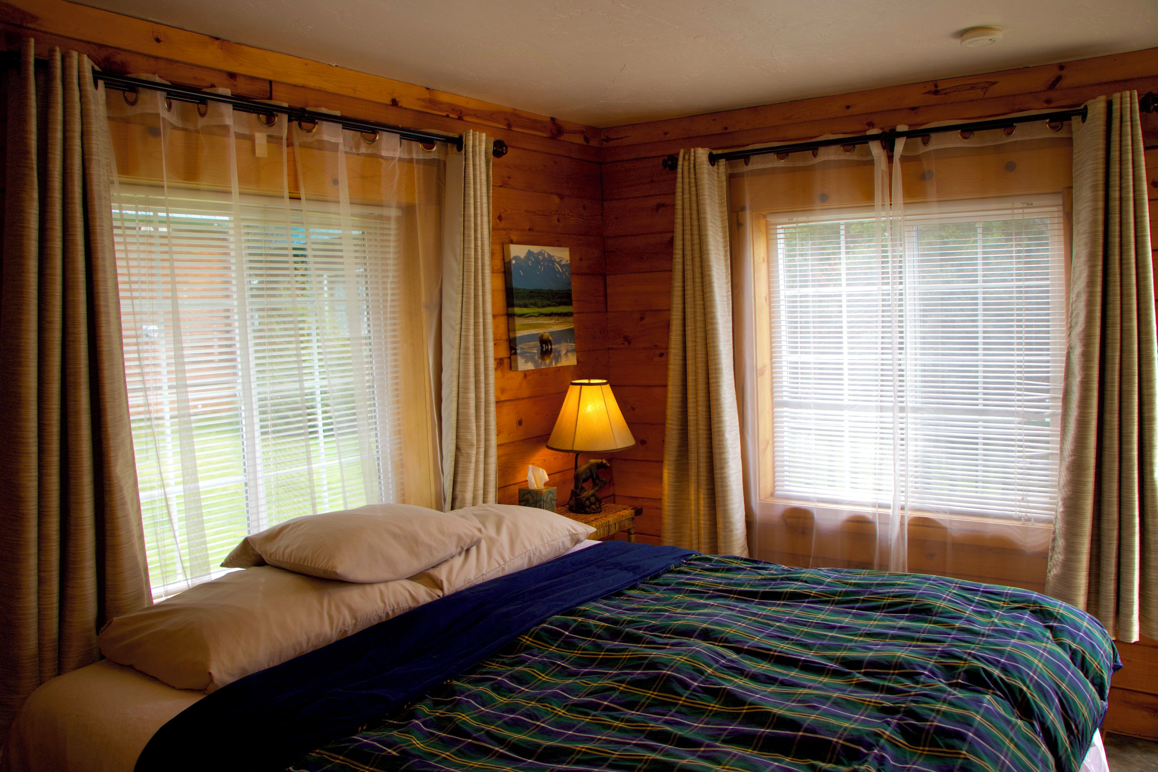 A room with a bed, curtains, a lamp, and a painting on the wall.