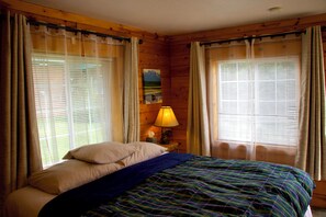 A room with a bed, curtains, a lamp, and a painting on the wall.