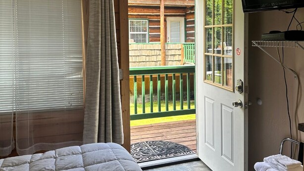 Habitación de cabaña de madera con una cama, una puerta que da a un balcón y un televisor montado en la pared.