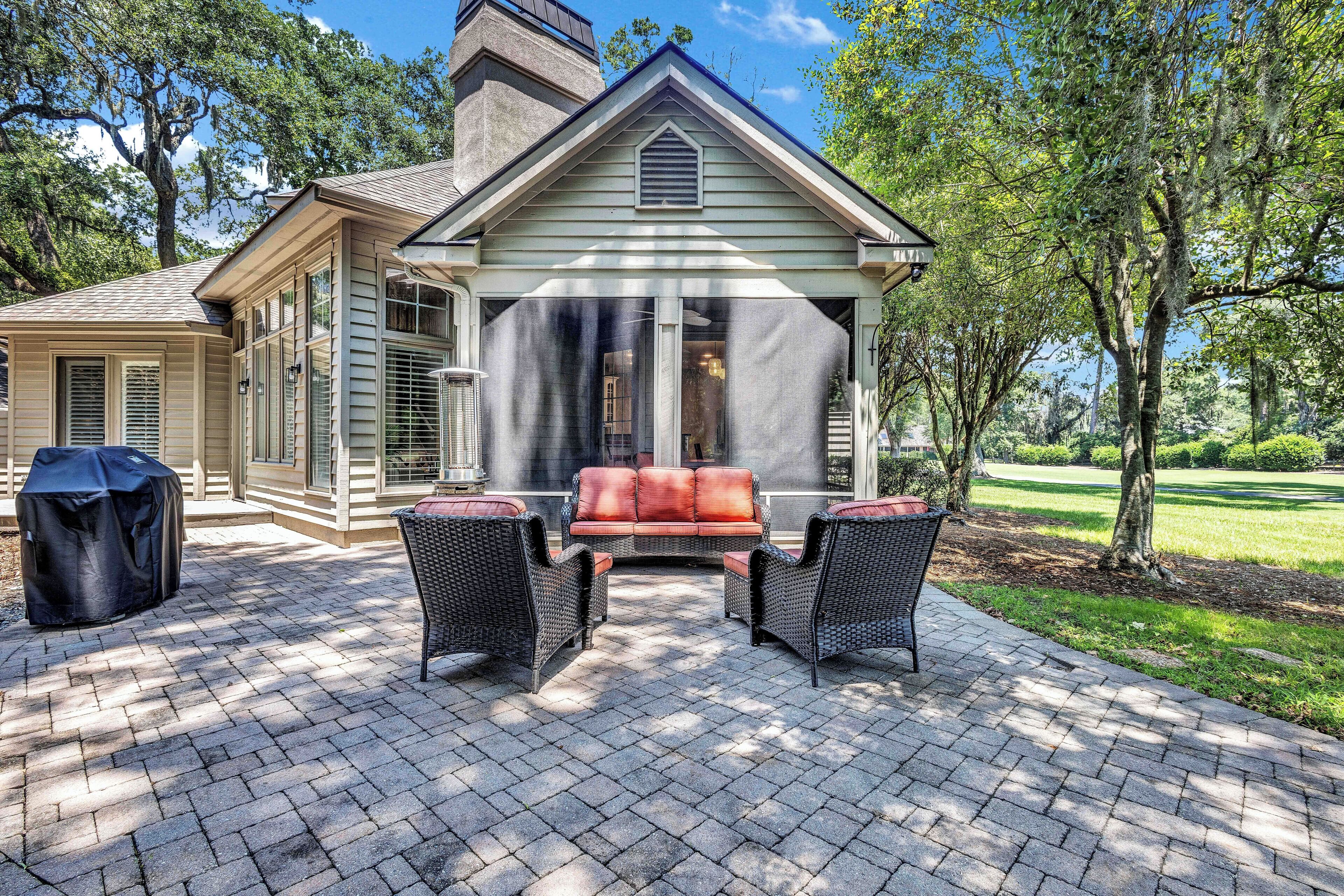 A covered patio with a brick floor, outdoor furniture, and a view of a house with a chimney.