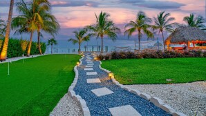 A pathway leading to a beach with palm trees and a thatched-roof structure.