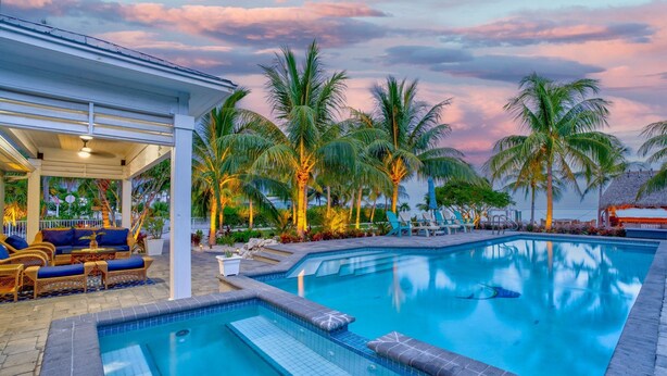 A swimming pool with a lounge area, palm trees, and a covered seating area.
