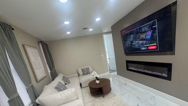 A modern living room with a sectional sofa, a coffee table, a flat-screen TV mounted on the wall, and a fireplace below it. - BEAUTIFUL FULLY RENOVATED 3 BEDROOM APARTMENT (West New York)
