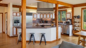 Une cuisine moderne avec des poutres en bois, un îlot central doté de tabourets et une vue sur l’extérieur.