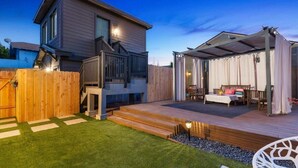 Een modern huis met twee verdiepingen, een houten terras en een overdekte zithoek buiten.