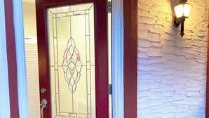 Una puerta roja con un panel de vidrio decorativo, una pared de ladrillo blanco y una lámpara fijada a la pared.