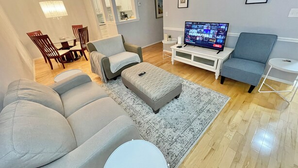 Una sala de estar moderna con un sofá gris, un sillón azul, una mesa de centro y un televisor sobre un soporte blanco.