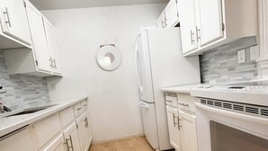 Una cocina moderna con armarios blancos, horno empotrado y refrigerador.