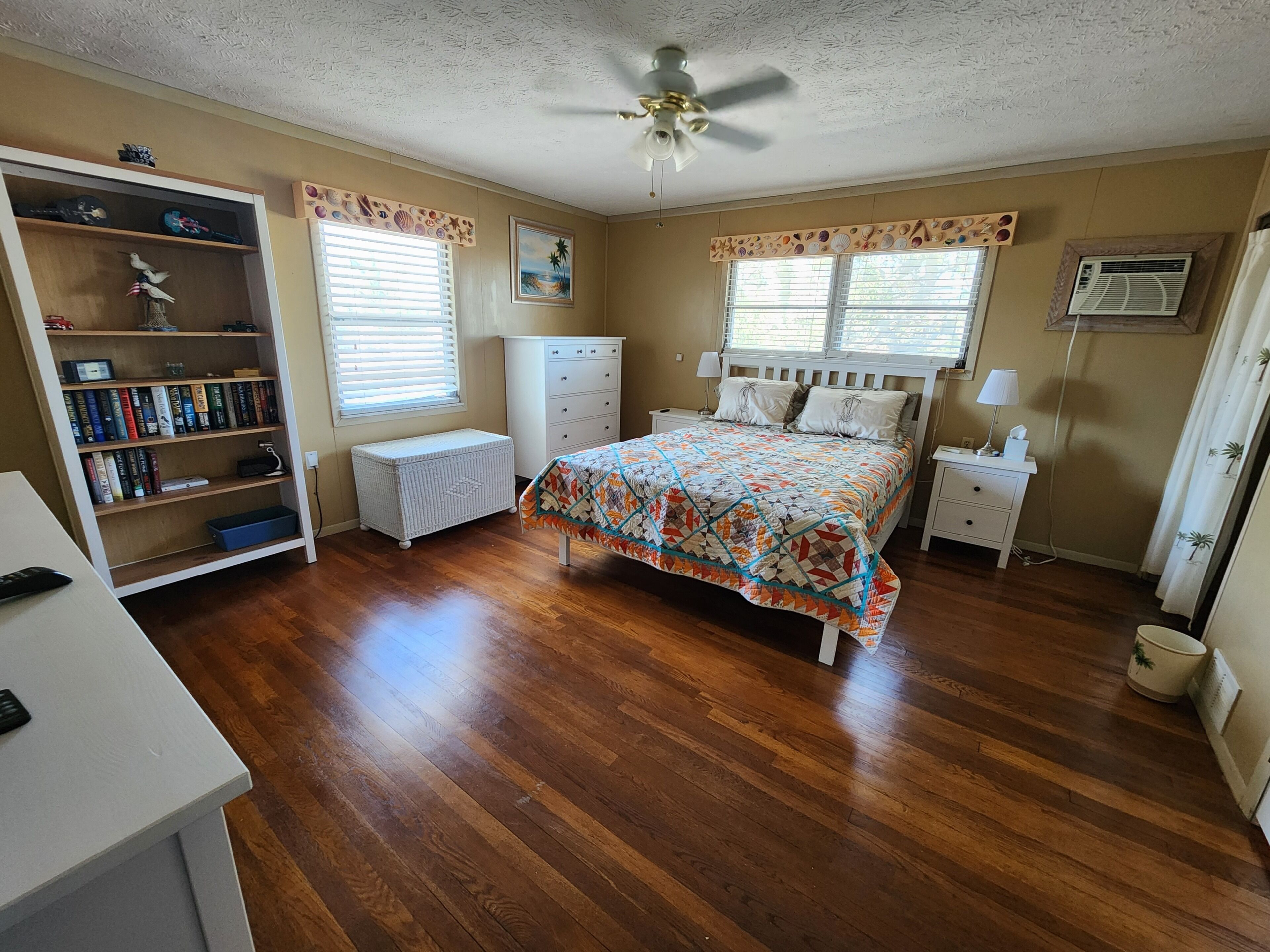 A bedroom with a bed, a bookshelf, a desk, a ceiling fan, and a window with blinds.