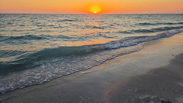 Ein Strand mit Wellen, einem Sonnenuntergang und einem klaren Himmel.