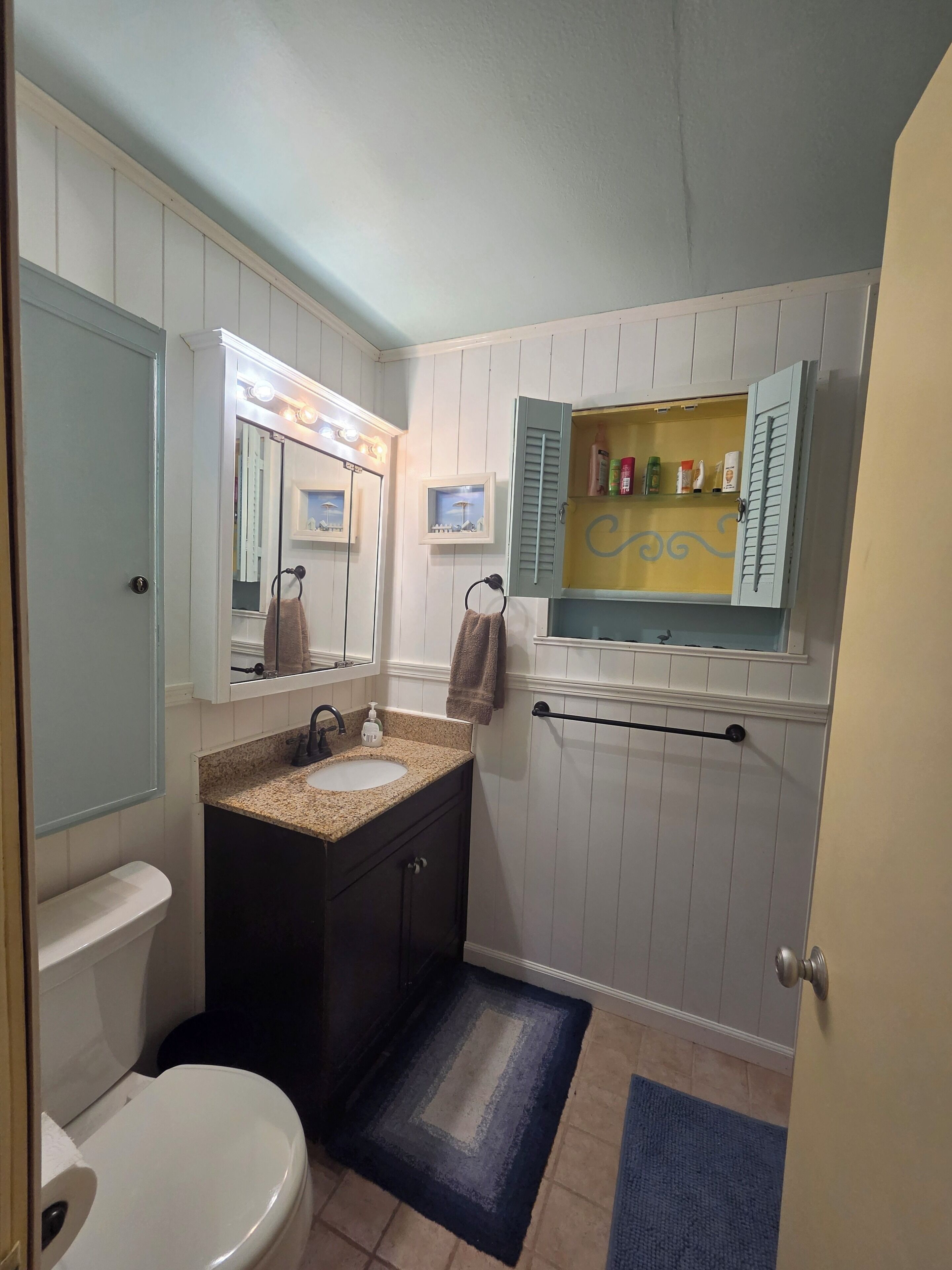 A bathroom with a sink, mirror, vanity, toilet, and towel rack.