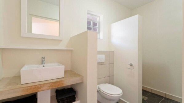 Un baño con lavamanos blanco, espejo, inodoro y zona de ducha.