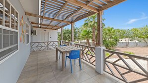 Eine überdachte Terrasse mit Holztisch und Stühlen, Blick auf die umliegende Landschaft und einem Geländer.