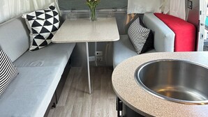 A compact RV interior with a kitchenette, a dining area, and a seating area with cushions. - Classic Airstream (Quincy)